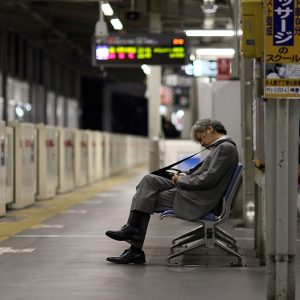 رجل في متوسط عمره ينام مرهقاً في انتظار القطار في طوكيو