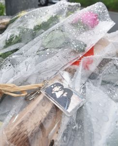 علاقة مفاتيح تحتوي على صورة أنمي انتجها استوديو كيوتو أنميشن مع أزهار وورد يقدمها الداعمون أثناء صلاتهم لأرواح الضحايا بالقرب من المبنى المحترق