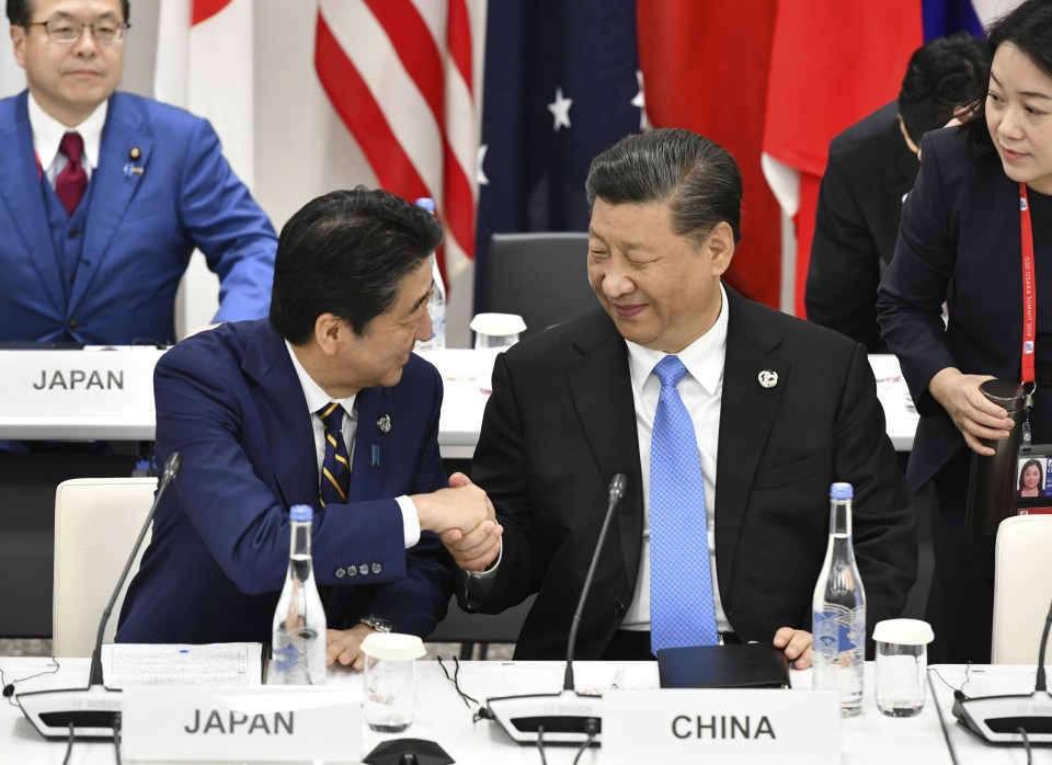 شينزو آبيه (يسارا) يصافح الزعيم الصيني شي جينبينغ (يمينا) خلال قمة مجموعة الـ20 في أوساكا عام 2019 | عبر كيودو