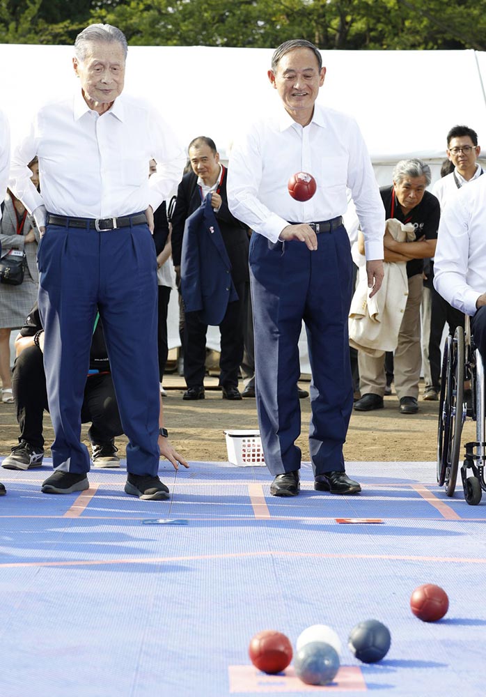 سوغا (يمين) يُجرب رياضة البوكا عام 2019 برفقة يوشيرو موري (يسار) رئيس الوزراء الأسبق، ترويجاً لألعاب طوكيو البارلمبية 2020 | عبر مكتب رئيس الوزراء الياباني وكيودو